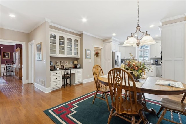 dining area with ornamental molding, built in desk, and light hardwood / wood-style flooring