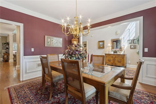 dining area with hardwood / wood-style flooring, ornamental molding, and an inviting chandelier