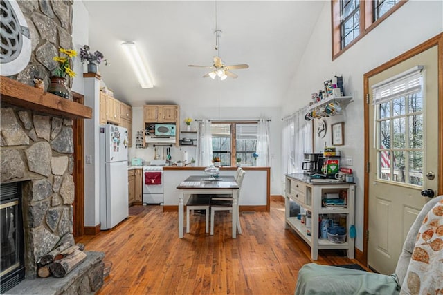 kitchen featuring ceiling fan, vaulted ceiling, white appliances, light hardwood / wood-style flooring, and a stone fireplace