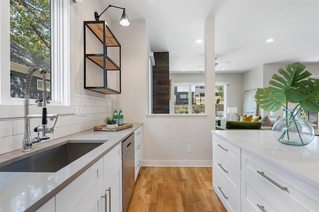 kitchen featuring tasteful backsplash, dishwasher, light hardwood / wood-style floors, white cabinets, and light stone counters