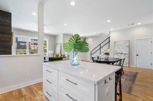 kitchen with light wood-type flooring, white cabinets, a kitchen bar, and a kitchen island