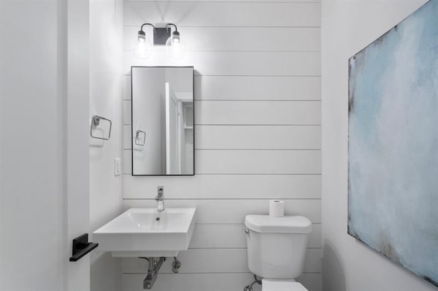 bathroom with toilet, wooden walls, and sink