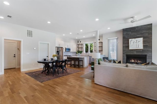 living room featuring ceiling fan, light wood-type flooring, and a large fireplace