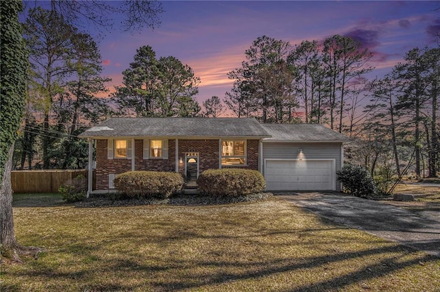 bi-level home featuring fence, driveway, a front lawn, a garage, and brick siding