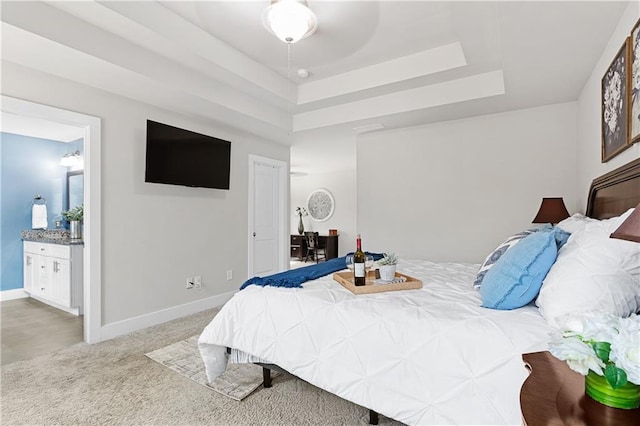 carpeted bedroom featuring a tray ceiling, baseboards, and ensuite bathroom