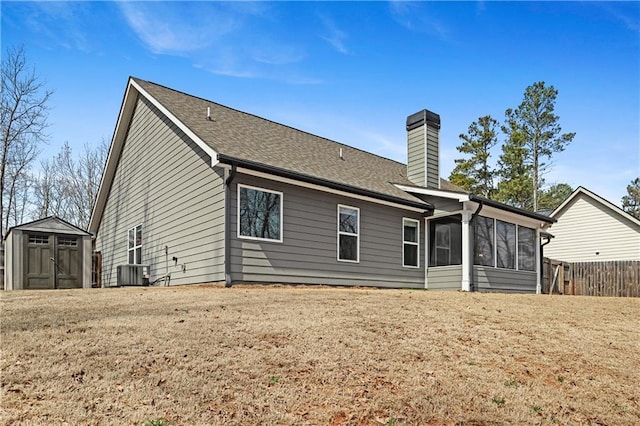 rear view of property featuring an outbuilding, fence, a shed, a sunroom, and a chimney