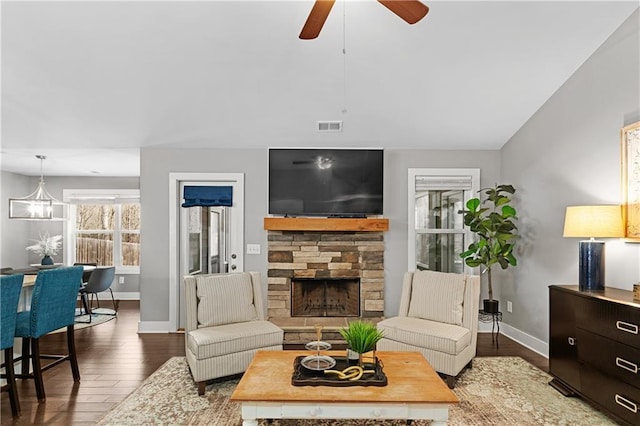 living area featuring visible vents, wood finished floors, a stone fireplace, baseboards, and ceiling fan