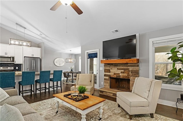 living area with visible vents, dark wood-type flooring, vaulted ceiling, a fireplace, and a ceiling fan