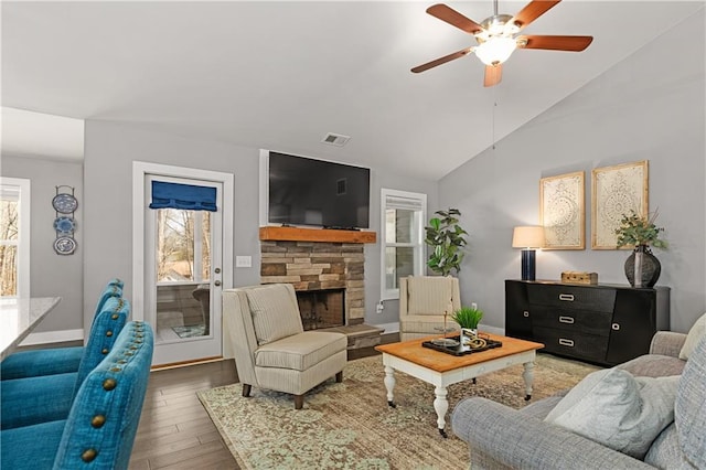 living area with visible vents, a ceiling fan, wood finished floors, a fireplace, and vaulted ceiling