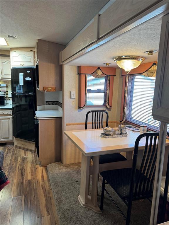 kitchen with black fridge, double wall oven, wood-type flooring, a textured ceiling, and a breakfast bar