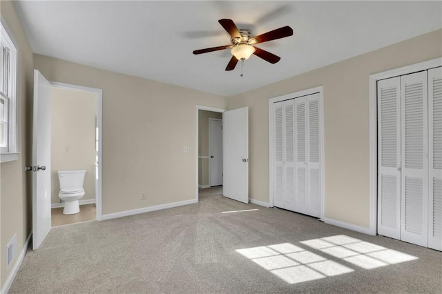 unfurnished bedroom with ensuite bath, ceiling fan, light colored carpet, and two closets