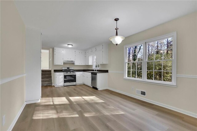 kitchen with white cabinets, stainless steel appliances, decorative light fixtures, and light hardwood / wood-style floors