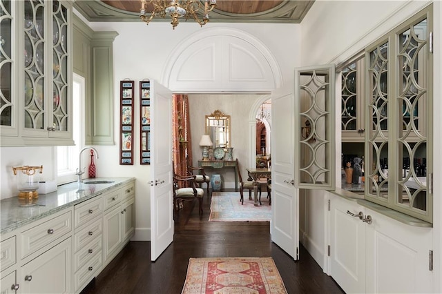 bar with light stone countertops, sink, dark wood-type flooring, white cabinets, and ornamental molding