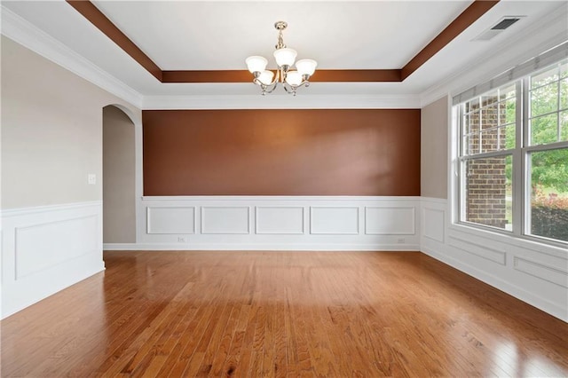 empty room with a notable chandelier, wood-type flooring, and a raised ceiling