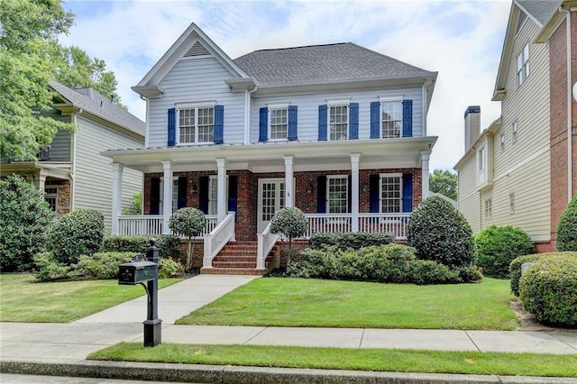 view of front facade featuring a porch, brick siding, a shingled roof, and a front lawn