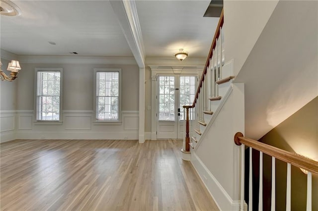 foyer entrance featuring a decorative wall, ornamental molding, wainscoting, light wood-type flooring, and stairs