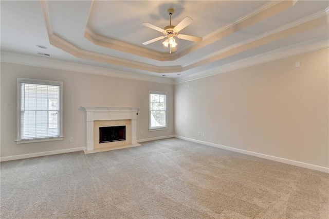 unfurnished living room with light carpet, baseboards, ornamental molding, a tray ceiling, and a fireplace