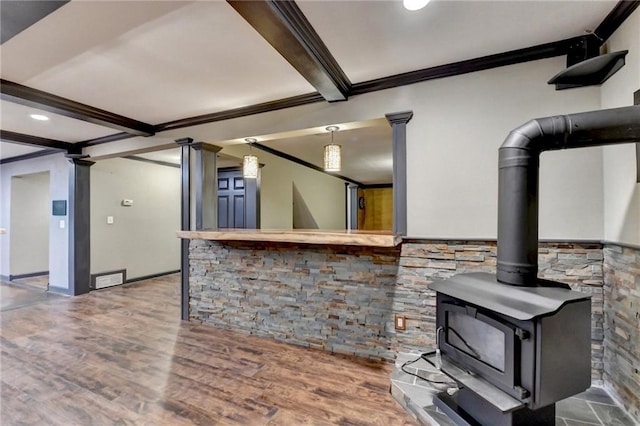 kitchen with crown molding, wood finished floors, beamed ceiling, a wood stove, and ornate columns