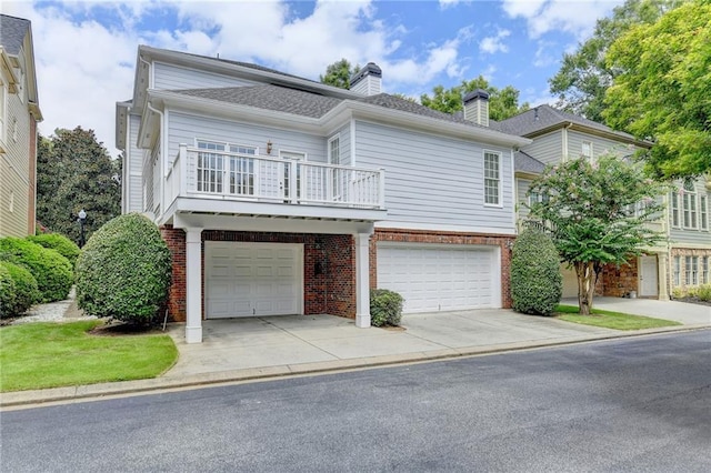 view of front of home featuring a garage, driveway, a balcony, a chimney, and brick siding