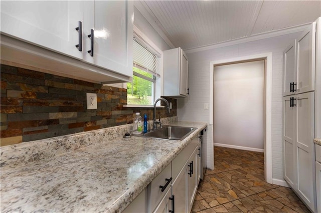 kitchen featuring a sink, stone finish flooring, backsplash, and white cabinets