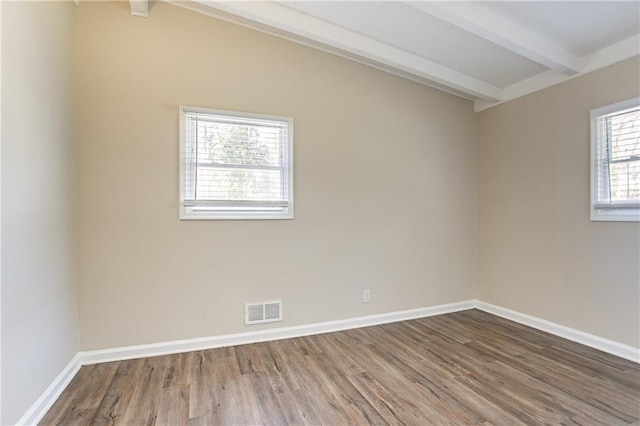 unfurnished room with visible vents, beamed ceiling, baseboards, and wood finished floors