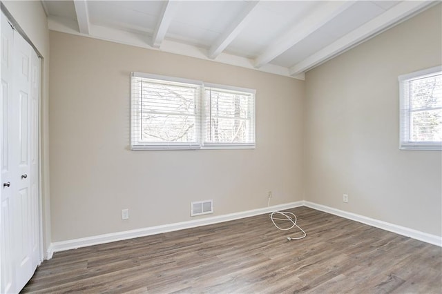 unfurnished bedroom with visible vents, baseboards, lofted ceiling with beams, wood finished floors, and a closet