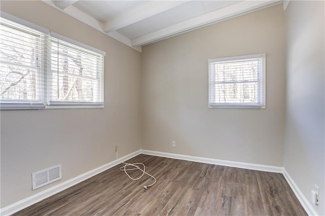 spare room with visible vents, beam ceiling, baseboards, and wood finished floors