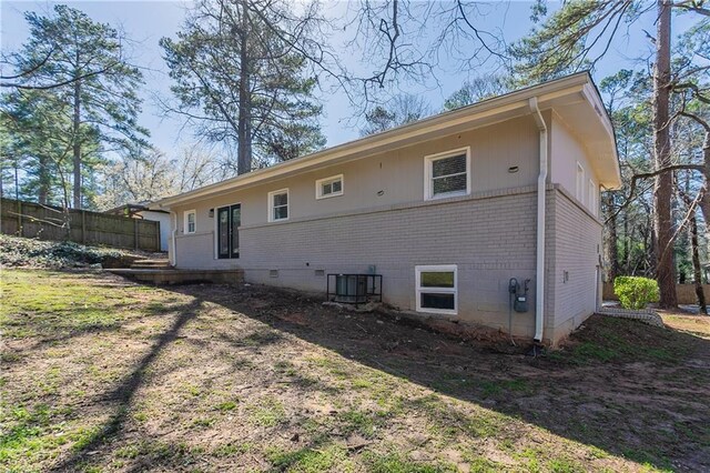 rear view of property featuring brick siding, crawl space, central AC, and fence