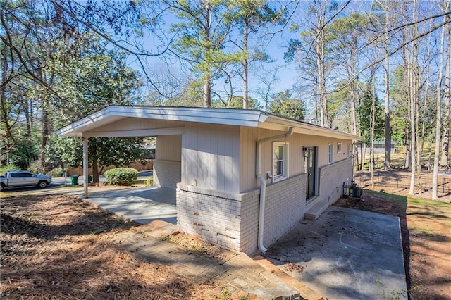 view of side of property featuring an attached carport, brick siding, and concrete driveway