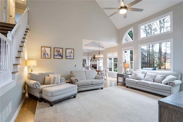 living room featuring plenty of natural light, ceiling fan with notable chandelier, wood-type flooring, and high vaulted ceiling