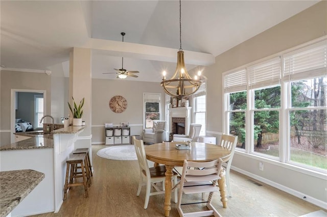 dining room with vaulted ceiling, a brick fireplace, sink, light hardwood / wood-style flooring, and ceiling fan with notable chandelier