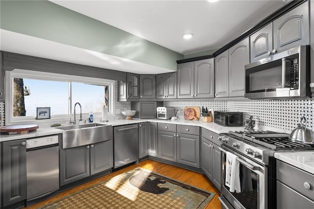 kitchen with stainless steel appliances, light countertops, backsplash, light wood-style flooring, and a sink