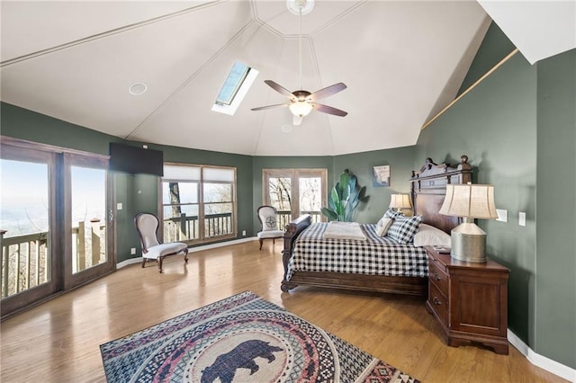 bedroom featuring access to exterior, ceiling fan, vaulted ceiling with skylight, and hardwood / wood-style floors