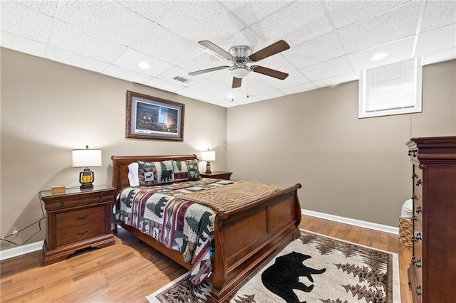 bedroom with wood-type flooring, a drop ceiling, and ceiling fan