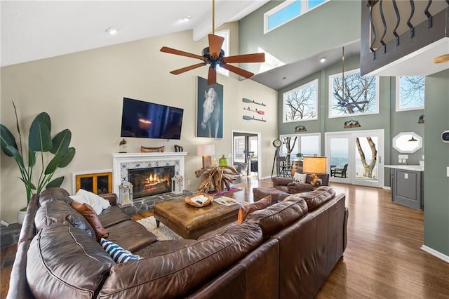 living room with beamed ceiling, hardwood / wood-style flooring, a stone fireplace, high vaulted ceiling, and ceiling fan