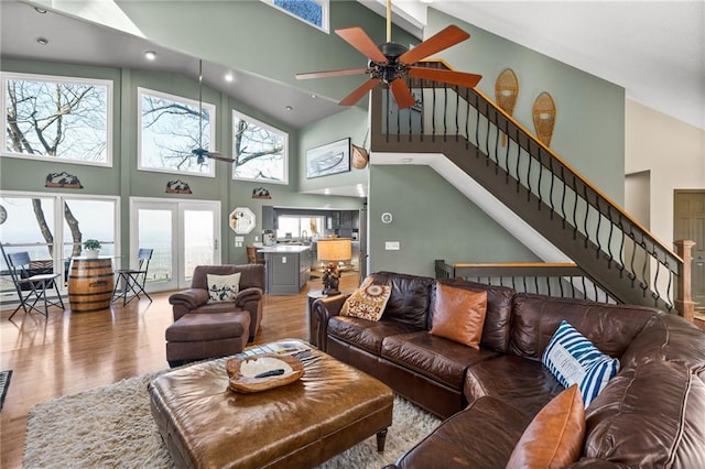 living area with light wood-style floors, ceiling fan, stairway, and high vaulted ceiling