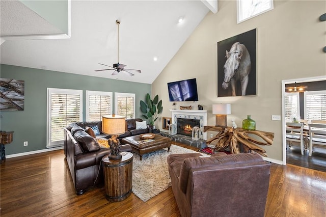 living area with dark wood-style floors, a stone fireplace, high vaulted ceiling, beamed ceiling, and baseboards