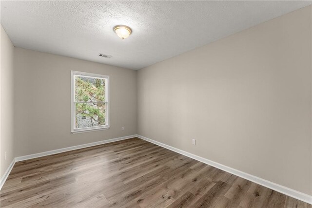 empty room featuring a textured ceiling, baseboards, and wood finished floors