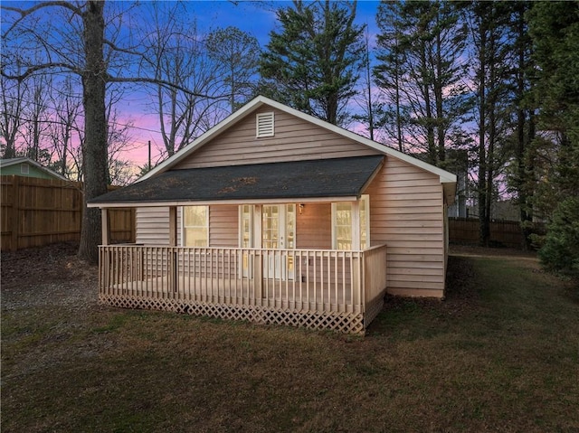 back house at dusk featuring a wooden deck and a lawn