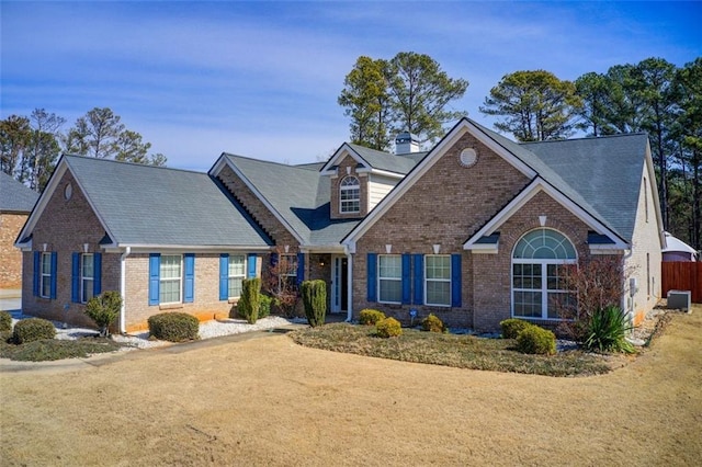 view of front of property with a chimney, fence, cooling unit, and brick siding