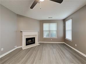 unfurnished living room featuring wood finished floors, ceiling fan, baseboards, and a fireplace with raised hearth
