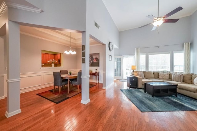 living area featuring visible vents, crown molding, light wood-type flooring, ceiling fan with notable chandelier, and a decorative wall