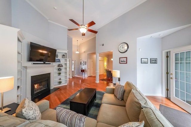 living area featuring wood finished floors, a ceiling fan, visible vents, high vaulted ceiling, and a fireplace with flush hearth