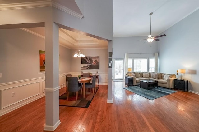 dining area with ceiling fan with notable chandelier, wood finished floors, a high ceiling, wainscoting, and crown molding