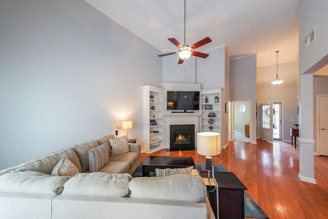 living area with visible vents, high vaulted ceiling, a ceiling fan, a warm lit fireplace, and wood finished floors