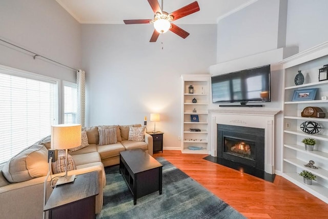 living room with wood finished floors, a fireplace with flush hearth, a ceiling fan, and ornamental molding