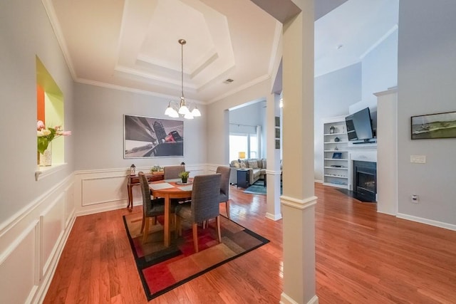 dining space with wood finished floors, crown molding, a raised ceiling, a decorative wall, and a notable chandelier