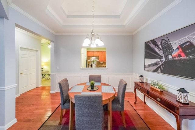 dining room with a tray ceiling, a notable chandelier, wood finished floors, and wainscoting