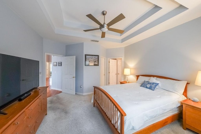 carpeted bedroom featuring visible vents, a ceiling fan, baseboards, a high ceiling, and a raised ceiling