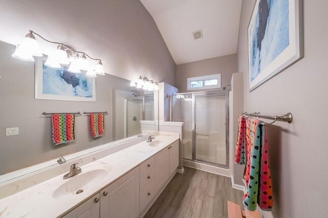 full bath with a stall shower, a sink, wood finished floors, double vanity, and vaulted ceiling